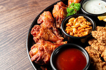 A delicious platter featuring crispy chicken wings, roasted peanuts, and dipping sauces, all elegantly arranged on a black plate and set on a wooden table.