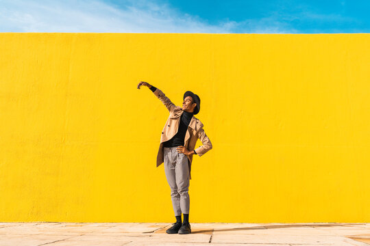 Young man dancing in front of yellow wall, taking selfies