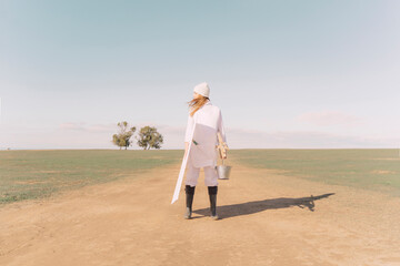 Young woman carrying easel and empty canvas on dry field