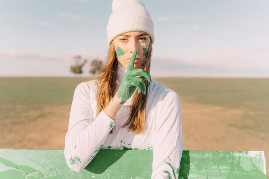Young woman putting finger of green hand on her mouth