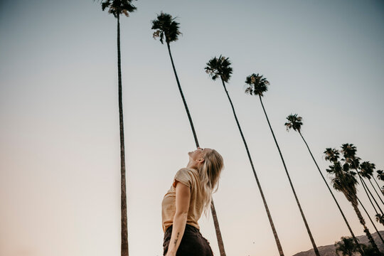 Low angle view of young woman under palm trees