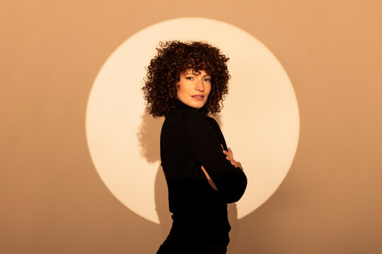 Woman standing with arms crossed against beige background