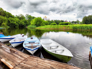 Obraz premium Boats lined up by the tranquil river under cloudy skies near a historic site