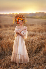 Obraz premium Beautiful girl in beige transparent summer dress and crown of flowers and ears on her head, walking through wheat field at sunset. Art photography. Autumn landscape.