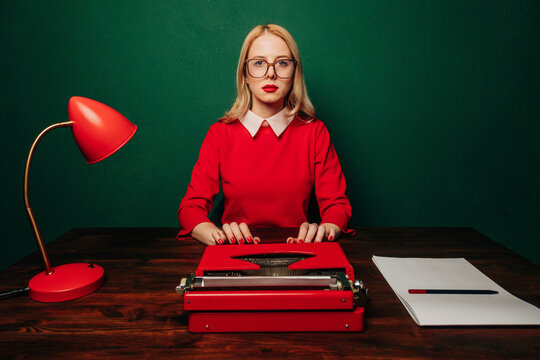 Stylish woman in red dress typing on a typewriter at a desk with a green background