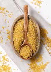 Raw dry uncooked yellow bulgur grain in a wooden spoon on a bowl topview. Ancient food