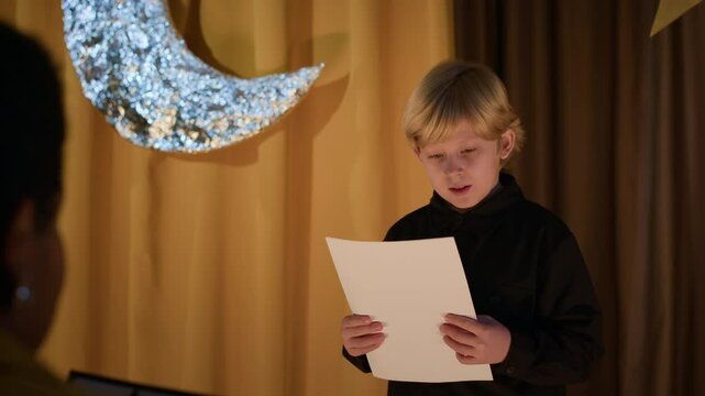 Over shoulder shot of Caucasian schoolboy standing on stage, reading script during audition in theatre