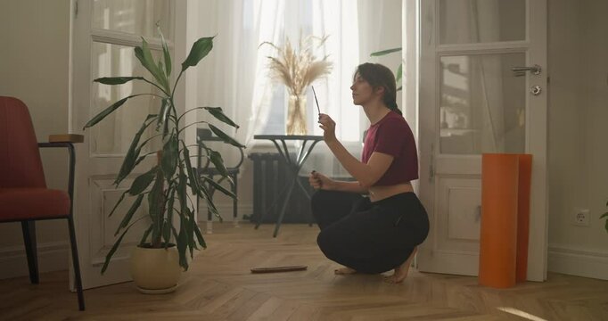 A brunette girl in a Red T-shirt lights incense before starting meditation at home