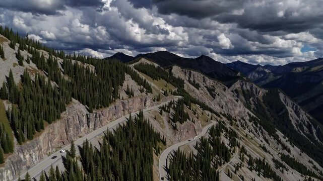 Mountain Road Serpentine: Captivating aerial view of a winding mountain road, etched into the rugged terrain, framed by towering peaks under a dramatic sky.