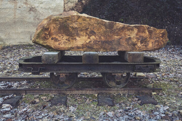 Heavy rock resting on an old mining cart beside railway tracks in a desolate area