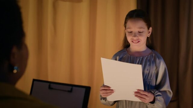 Over shoulder shot of cheerful Caucasian girl standing on stage, reading script during audition in school theatre