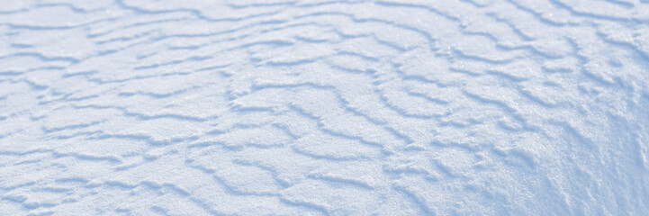 Beautiful winter background with snowy ground. Natural snow texture. Wind sculpted patterns on snow surface. Wide panoramic texture for background and design.