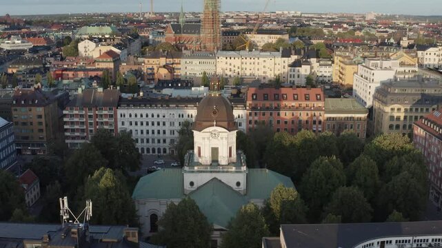 Drone shot of Adolf Fredriks church in Stockholm, Sweden during sunset in late summer. Shot pushing away from the church revealing buildings and Sveav&auml;gen in background.