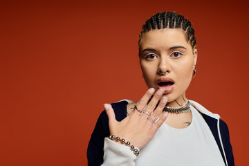 Stylish young woman expresses surprise against a vibrant orange backdrop in urban setting