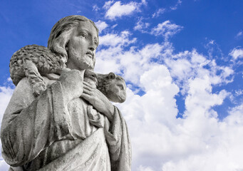 Jesus Christ the good shepherd holds a lost sheep on his shoulders against a blue sky background