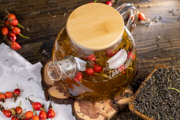 red rosehip fruits and hot green tea in a transparent teapot