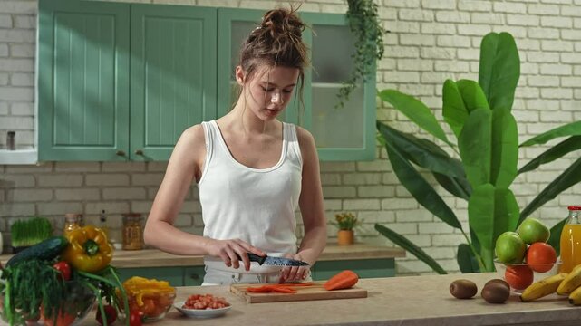 Young woman at the table in the kitchen preparing spring rolls for healthy lunch, woman cutting carrot with knife on slices. Slow motion.