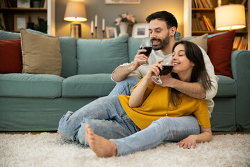 Fototapeta premium An engaging moment with a couple on the floor, sharing wine and smiles, showcasing the warmth of their emotional connection.