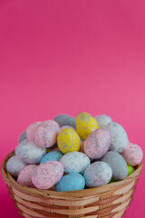 On a purple background, a wicker basket filled with Easter colorful eggs is located at the bottom of the photo, with a place for text, advertising or congratulations on top. Vertical photography. The 