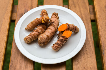 Fresh turmeric rhizomes on dish on wooden table