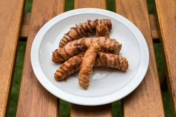 Fresh turmeric rhizomes on dish on wooden table