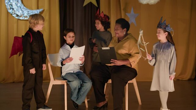 Wide shot of senior African American woman working with group of kids in school theater