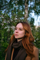 Naklejka premium portrait of a young woman looking to the side against a background of flowering trees on a spring day. A walk in the spring park