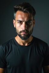 Fototapeta premium Serious bearded man with short hair and black t-shirt posing in studio with dark background