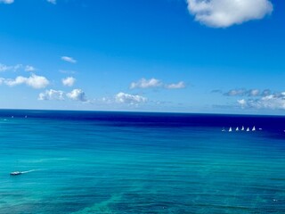 Wide open turquoise ocean view with small white sailboats in the background