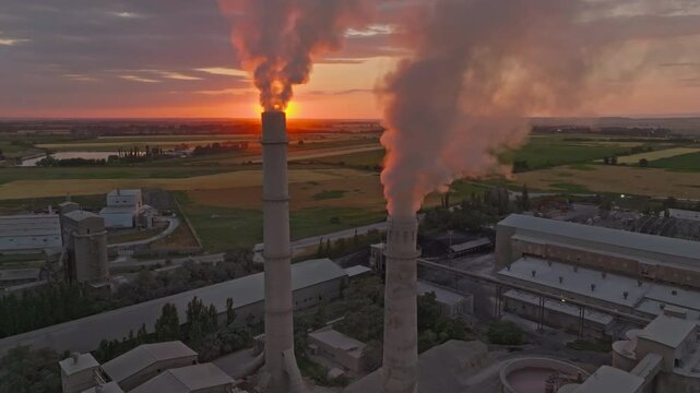 setting sun behind of smoke and steam out of soviet concrete factory pipe, aerial view