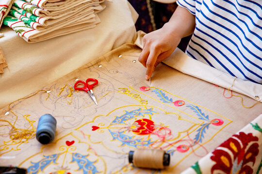 In Tashkent, Uzbekistan, an artisan carefully hand-embroiders a vibrant floral pattern, surrounded by traditional Uzbek textiles. A glimpse into Uzbek craftsmanship heritage.
