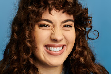 Emotional expression of a young stylish woman with curly hair against a blue backdrop