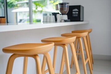 A minimalist coffee shop with light wood barstools, white walls, and large windows, showcasing the sleek design of its counter in natural lighting