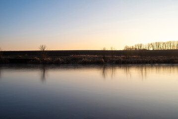 Bank of frozen river at sunset with bare trees