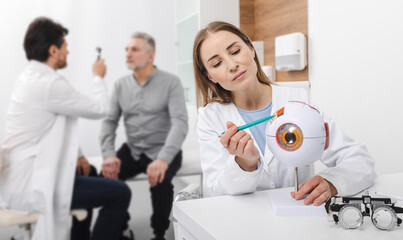 Optometrist demonstrating eye anatomy during patient consultation in clinical setting. Vision...