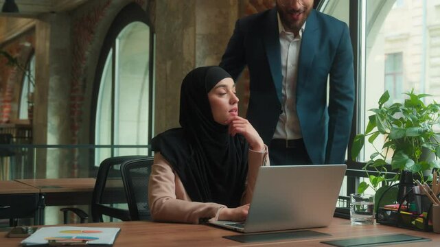 Arabian Indian man boss businessman come help Muslim businesswoman laptop work in office two coworkers discuss computer project mentor help intern woman in hijab advice consult multiethnic teamwork