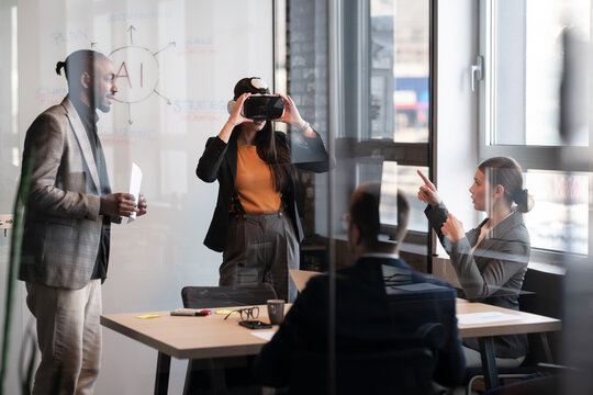 Business professionals in a modern office collaborate on an AI project. Woman explores virtual reality while colleagues discuss strategies. Concept of innovation and technology in the workplace
