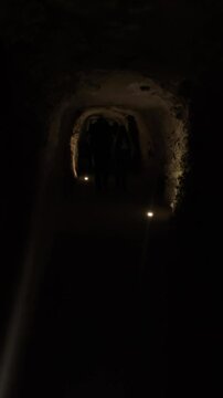 Exploring ancient underground tunnels illuminated by soft lights at night. A group of visitors navigates through dimly lit tunnels deep underground, surrounded by historic stone walls and a mysterious