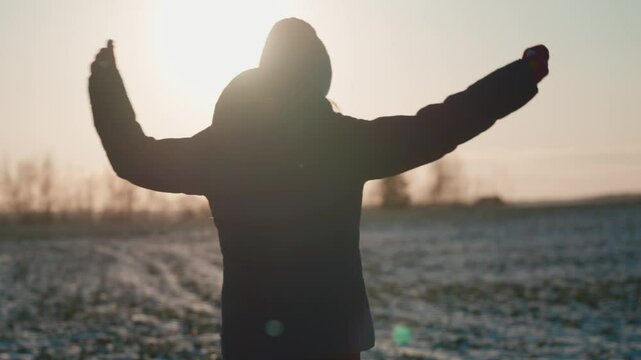 Backlit silhouette of young orphan girl walking through snowy field during golden sunset, capturing profound emotional landscape of childhood solitude and inner resilience. Kid spinning in winter 