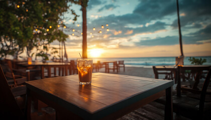 A beautifully captured image of an iced coffee sitting on a wooden table at a beachside caf&eacute; during sunset.