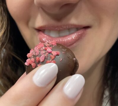 Closeup of a beautiful woman eating a chocolate truffle. Can represent Valentine's Day, chocolate shop, or self love. 