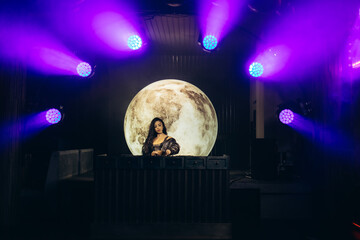 DJ Performing at Nightclub Stage with Moon Backdrop and Colorful Lighting