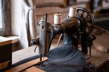An antique sewing machine with a weathered metal body and wooden spool holders sits in a rustic workshop.