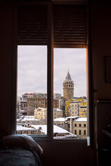View of snow-covered Istanbul from a cozy room with Galata Tower framed in the window. Travel and tourism concept.