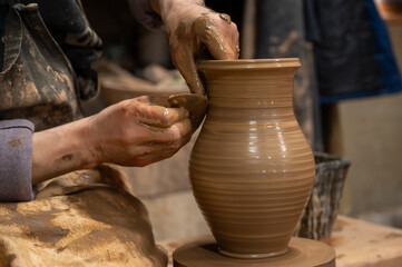 Close-up of a potter’s hands covered in wet clay as they carefully shape a ceramic vase on a pottery wheel.
