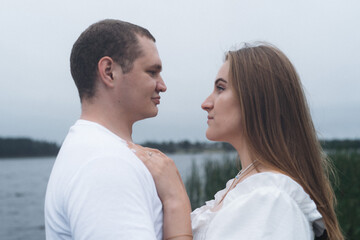 Romantic couple kissing and embracing near a lake and forest on a cloudy day.