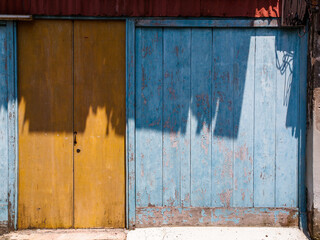 Old wooden blue walls and dark yellow wooden door with small steel handles and lock with shadows.