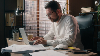 Stressed Caucasian guy manager executive male tired businessman worker man ceo leader broker working online in office typing laptop yawn exhaustion problem drinking coffee energy beverage cup business