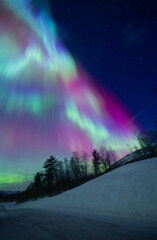 A beautigul autora borealis display over the snowy Norvegian winter landscape. Northern lights in Norway sky. Arctic nature in Scandinavia during winter season.