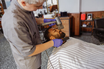 In a stylish salon adorned with vintage decor, a skilled barber meticulously trims and shapes a...